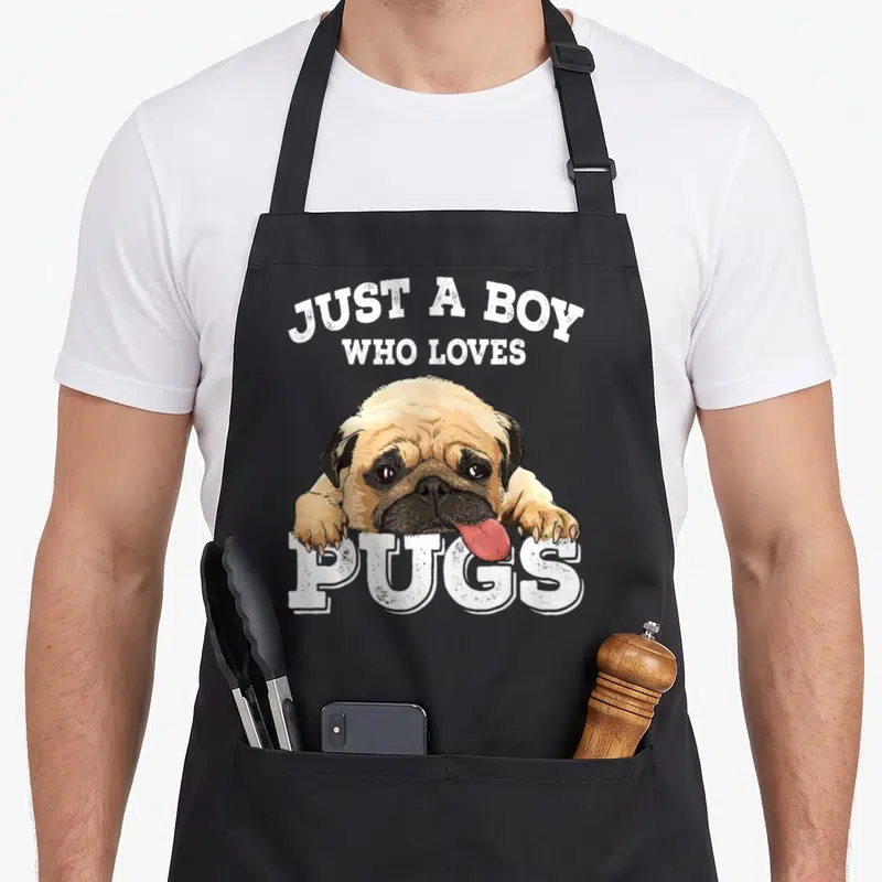 Vintage pug dog apron - Realistic tan and black pug resting paws on white Just a Boy Who Loves Pugs text — shown on a black cotton canvas apron against a white background