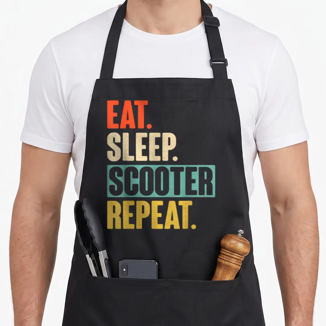 Eat scooter apron - Stacked red beige blue and yellow distressed text reading EAT SLEEP SCOOTER REPEAT — shown on a black cotton canvas apron against a white background