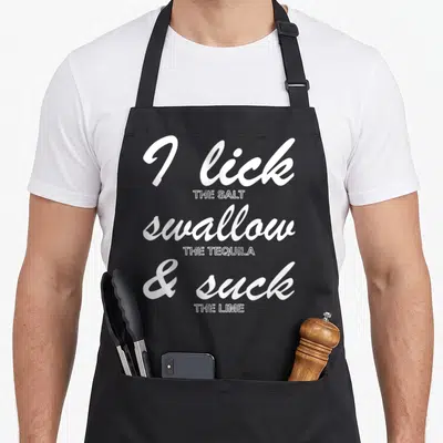 Funny drinking st patrick day aprons - White stacked typography reading I lick salt swallow tequila suck lime — shown on a black cotton canvas apron against a white background