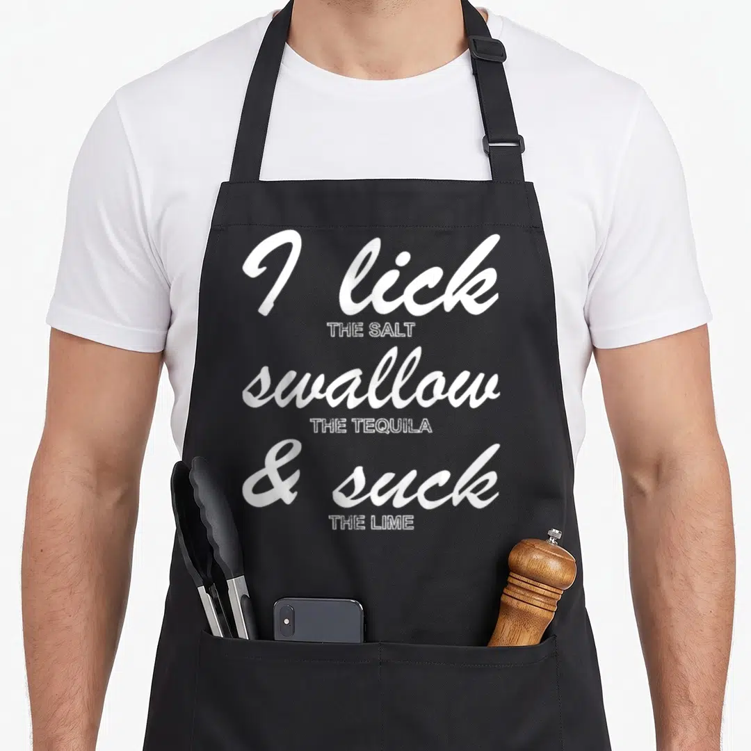 Funny drinking st patrick day aprons - White stacked typography reading I lick salt swallow tequila suck lime — shown on a black cotton canvas apron against a white background