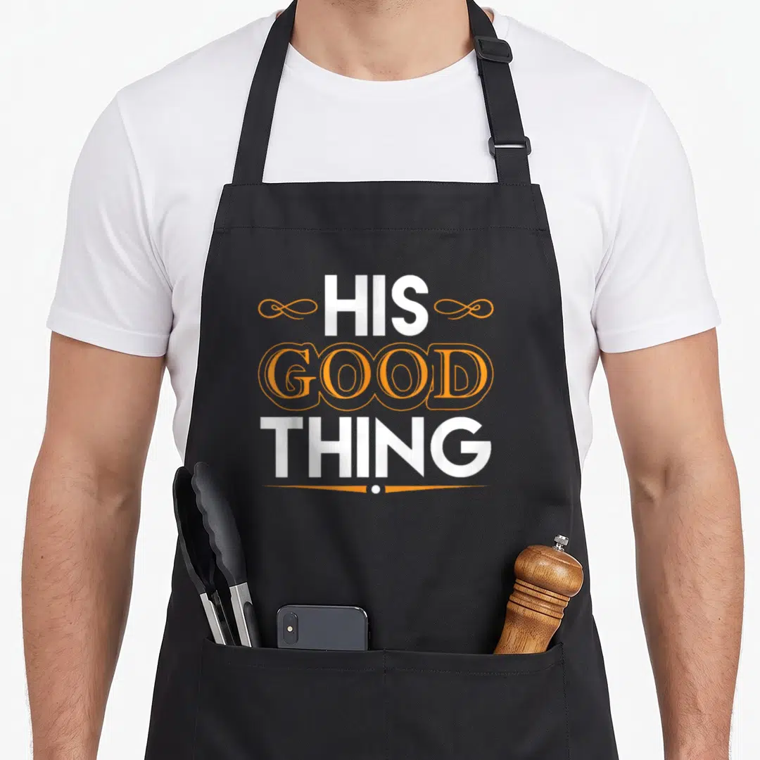 Find couple apron - Stacked white and orange text reading His Good Thing with swirls and a dot underline — shown on a black cotton canvas apron against a white background