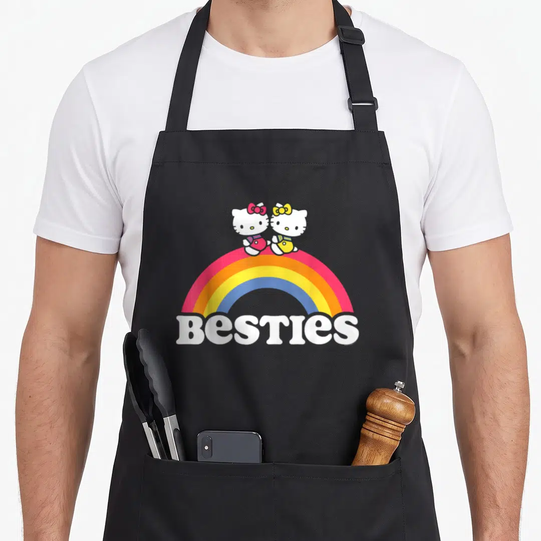Mimmy hello apron - Two cartoon cats on rainbow with BESTIES text in white — shown on a black cotton canvas apron against a white background