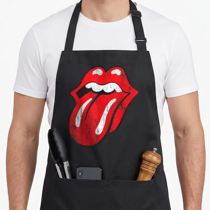 Distressed tongue rolling stones apron - Red white and black distressed mouth graphic with protruding tongue — shown on a black cotton canvas apron against a white background