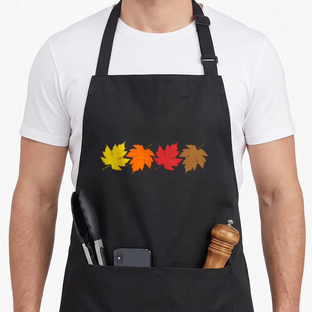 Leave fall aprons - Four maple leaves in yellow, orange, red, and brown arranged horizontally — shown on a black cotton canvas apron against a white background