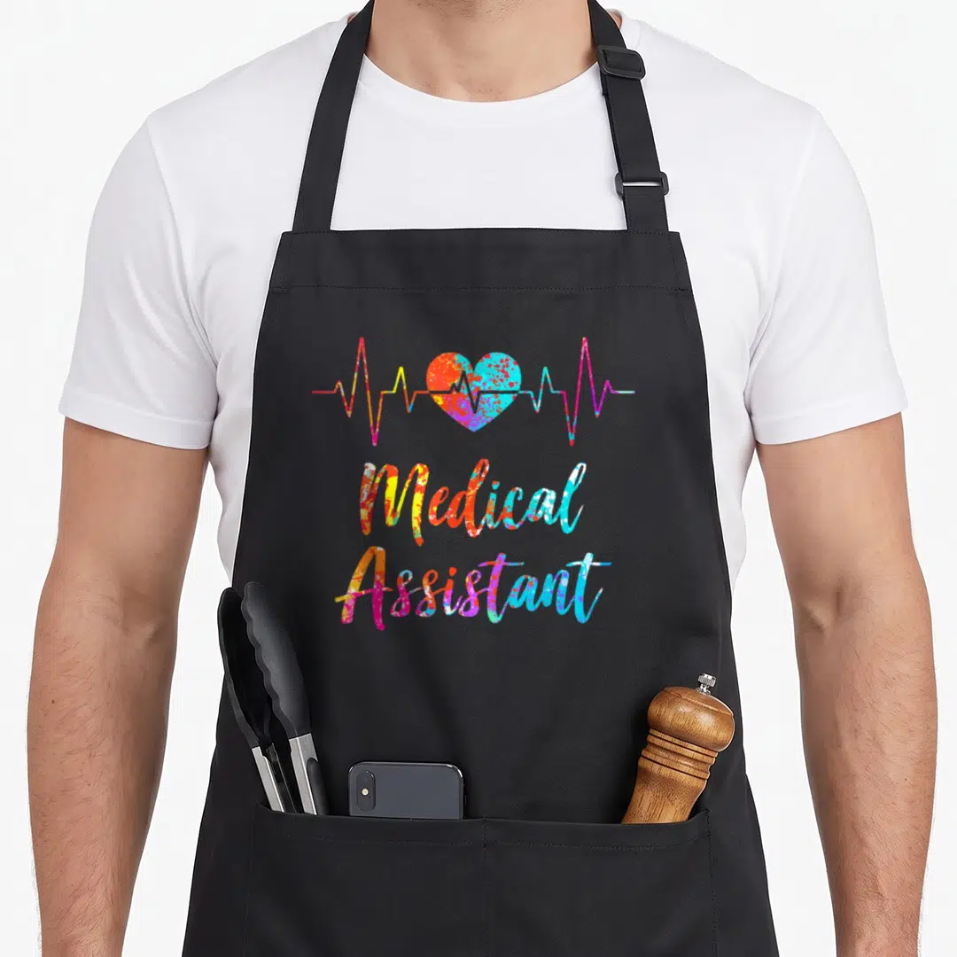 Medical nursing aprons - Tie-dye heartbeat line and Medical Assistant script in red yellow blue pink orange — shown on a black cotton canvas apron against a white background
