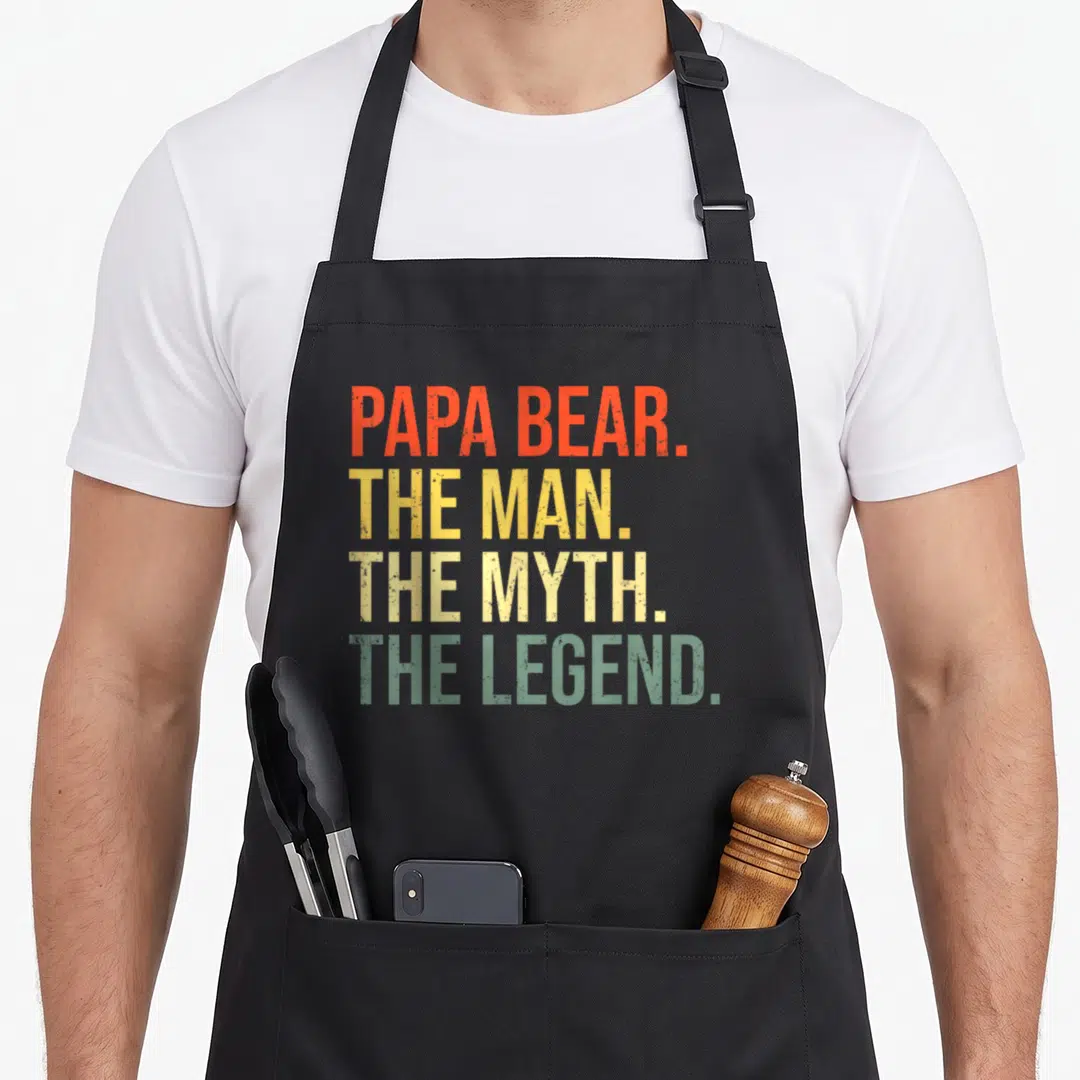 Bear myth father day apron - Stacked PAPA BEAR THE MAN THE MYTH THE LEGEND text in orange red and green — shown on a black cotton canvas apron against a white background