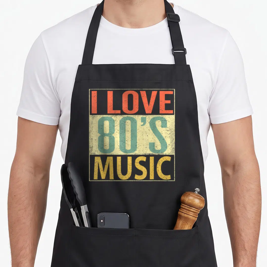 Music 80s apron - I LOVE 80'S MUSIC text in red teal yellow distressed typography on beige rectangle — shown on a black cotton canvas apron against a white background