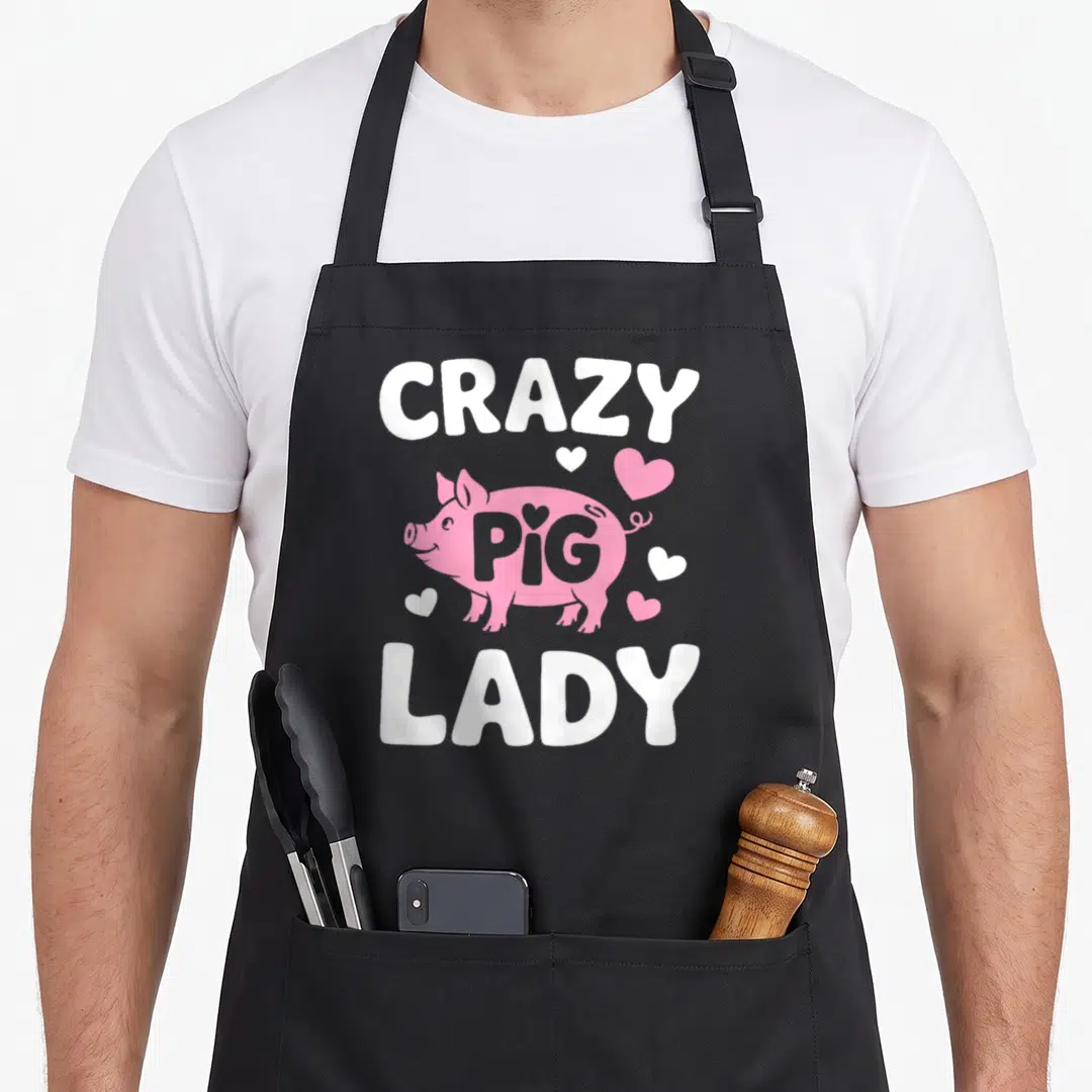 Obsessed pig lady apron - Pink cartoon pig with hearts and white text reading CRAZY PIG LADY — shown on a black cotton canvas apron against a white background