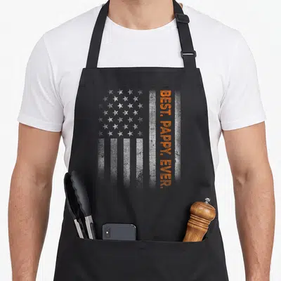 Pappy flag father day apron - Distressed white stars and orange vertical text reading BEST. PAPPY. EVER. over flag — shown on a black cotton canvas apron against a white background