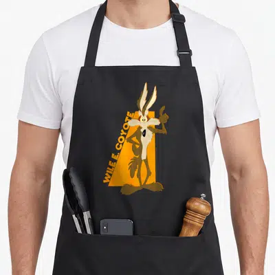 Wile simple apron - Wile E. Coyote cartoon character standing in front of orange shape with diagonal text — shown on a black cotton canvas apron against a white background