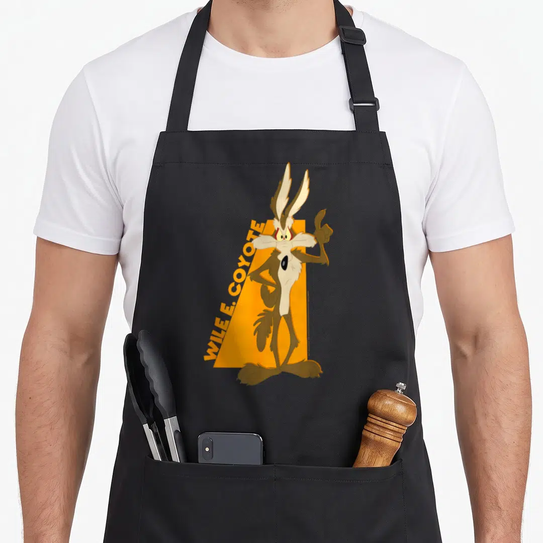 Wile simple apron - Wile E. Coyote cartoon character standing in front of orange shape with diagonal text — shown on a black cotton canvas apron against a white background