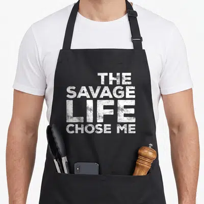 Chose savage apron - White stacked text reading THE SAVAGE LIFE CHOSE ME in distressed font — shown on a black cotton canvas apron against a white background