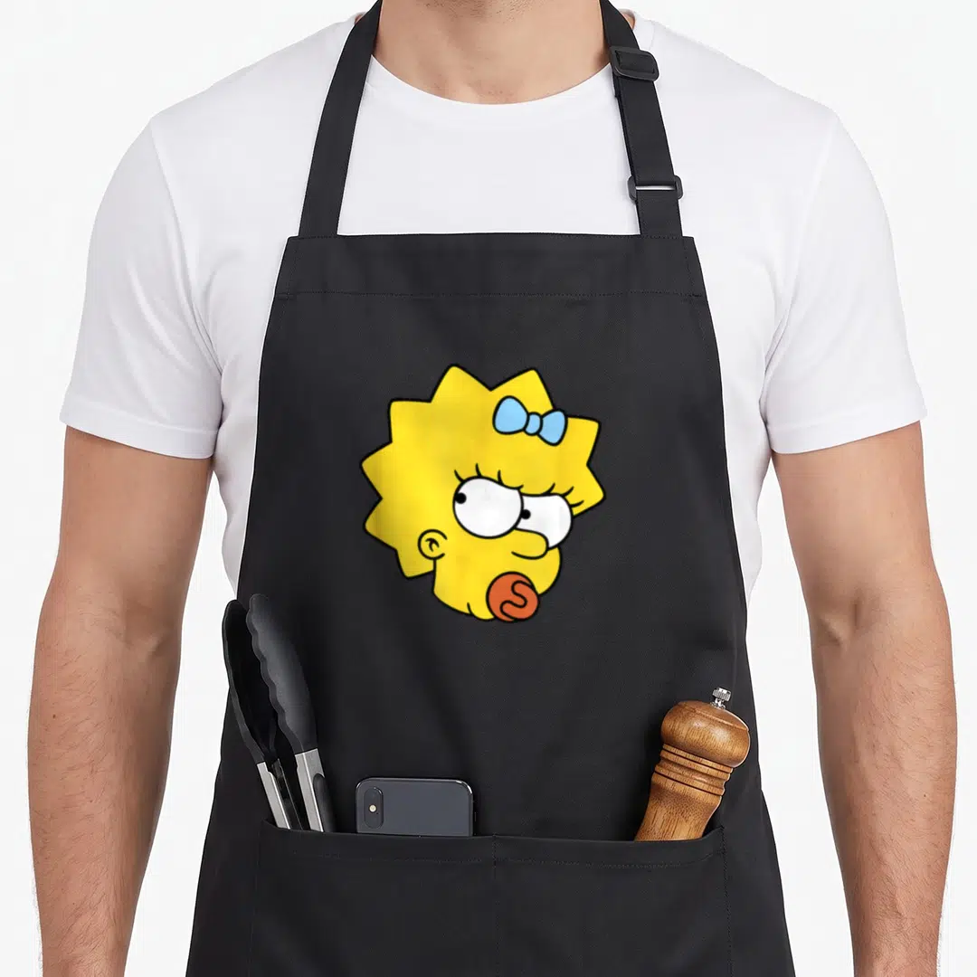 Maggie face apron - Yellow cartoon head with light blue bow and red S-shaped lollipop — shown on a black cotton canvas apron against a white background