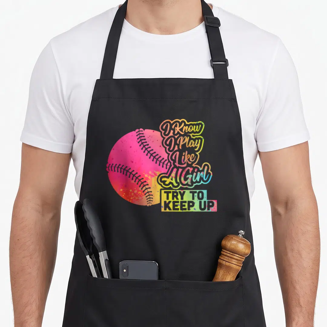 Play baseball apron - Multicolored watercolor softball next to stacked script text I Know I Play Like A Girl TRY — shown on a black cotton canvas apron against a white background
