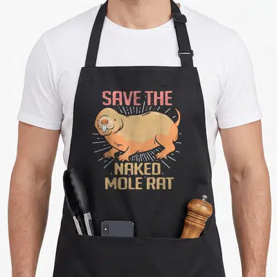 Naked rat mole apron - Cartoon tan and orange naked mole rat with SAVE THE NAKED MOLE RAT text and white rays — shown on a black cotton canvas apron against a white background