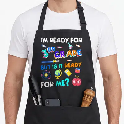3rd ready grade apron - I'm Ready for 3rd Grade text with crayons, globe, atom, and apple glasses in blue pink yellow — shown on a black cotton canvas apron against a white background