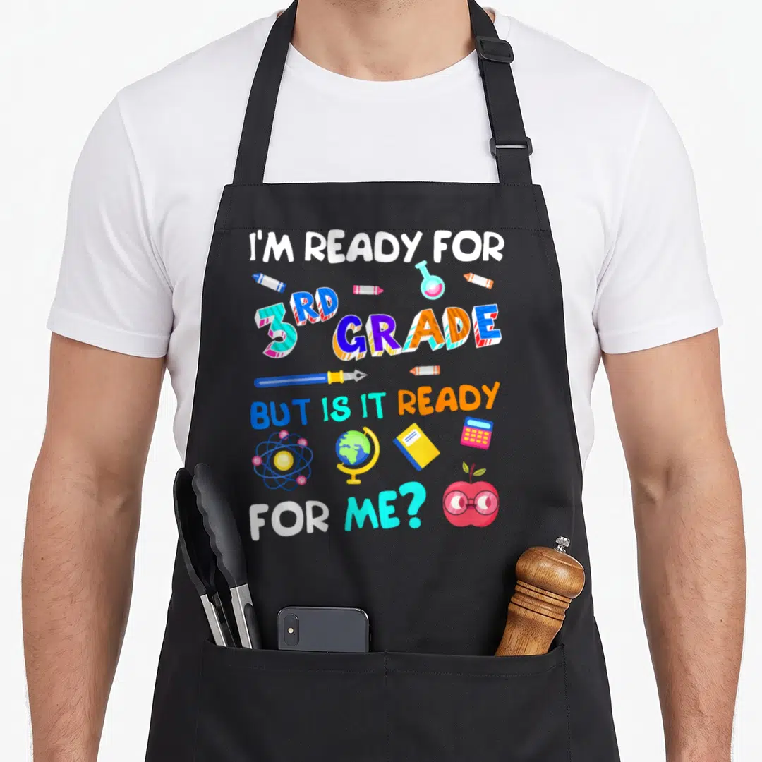 3rd ready grade apron - I'm Ready for 3rd Grade text with crayons, globe, atom, and apple glasses in blue pink yellow — shown on a black cotton canvas apron against a white background