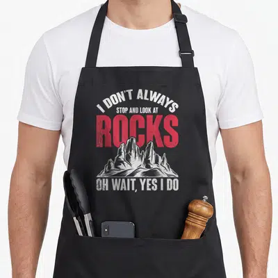Natural geologist humor apron - Distressed text I DON'T ALWAYS, STOP AND LOOK AT, ROCKS, OH WAIT, YES I DO with white — shown on a black cotton canvas apron against a white background