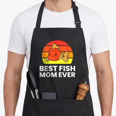 Cool fish apron - Cartoon orange fish on striped sunset circle with BEST FISH MOM EVER text below — shown on a black cotton canvas apron against a white background