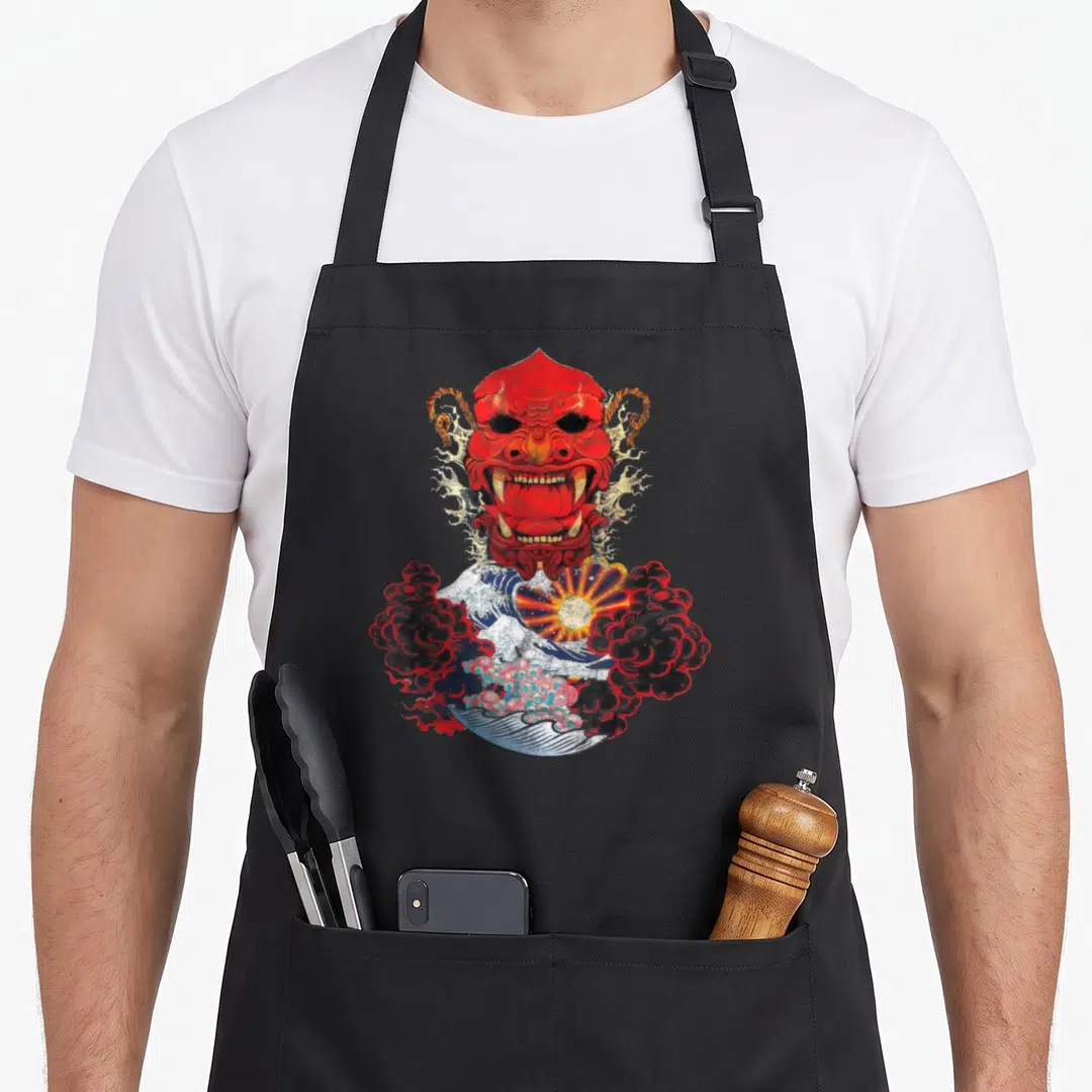 Japanese ogre apron - Red Hannya mask above blue wave and rising sun in black and yellow — shown on a black cotton canvas apron against a white background