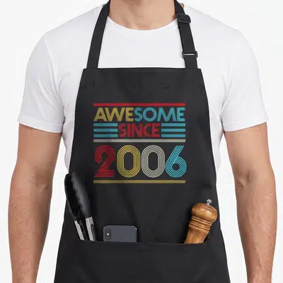 Cute 16th birthday apron - Stacked AWESOME SINCE 2006 text in red yellow white blue horizontal lines — shown on a black cotton canvas apron against a white background