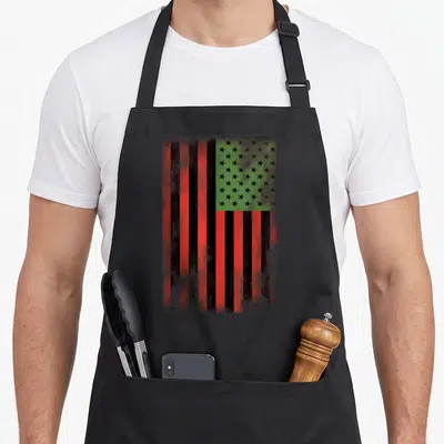 Flag african print apron - Distressed red black and green flag with black stars on green background — shown on a black cotton canvas apron against a white background