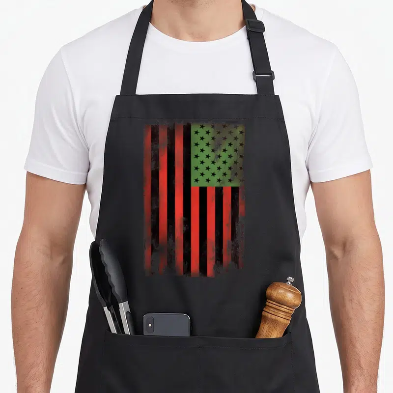 Flag african print apron - Distressed red black and green flag with black stars on green background — shown on a black cotton canvas apron against a white background