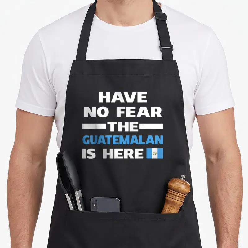 Proud guatemalan aprons - Stacked white and blue text reading Have No Fear The Guatemalan Is Here next to a small flag — shown on a black cotton canvas apron against a white background
