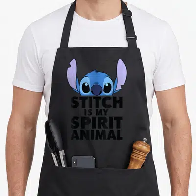 Funny animal apron - Blue Stitch head peeks over black text reading STITCH IS MY SPIRIT ANIMAL — shown on a black cotton canvas apron against a white background