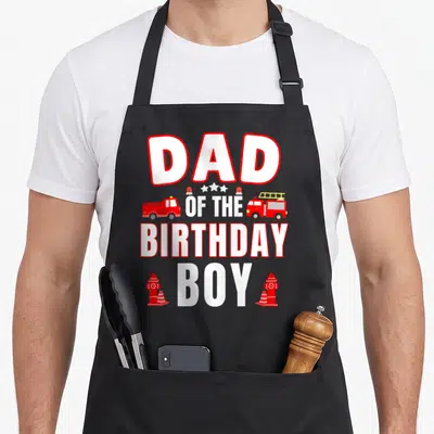 Fire firefighter aprons - Dad of the Birthday Boy text with red fire trucks and hydrants — shown on a black cotton canvas apron against a white background