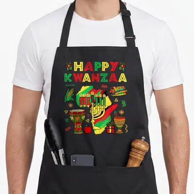 Kinara african american aprons - Cartoon Africa map with kinara, drum, corn, and HAPPY KWANZAA text in red yellow green — shown on a black cotton canvas apron against a white background