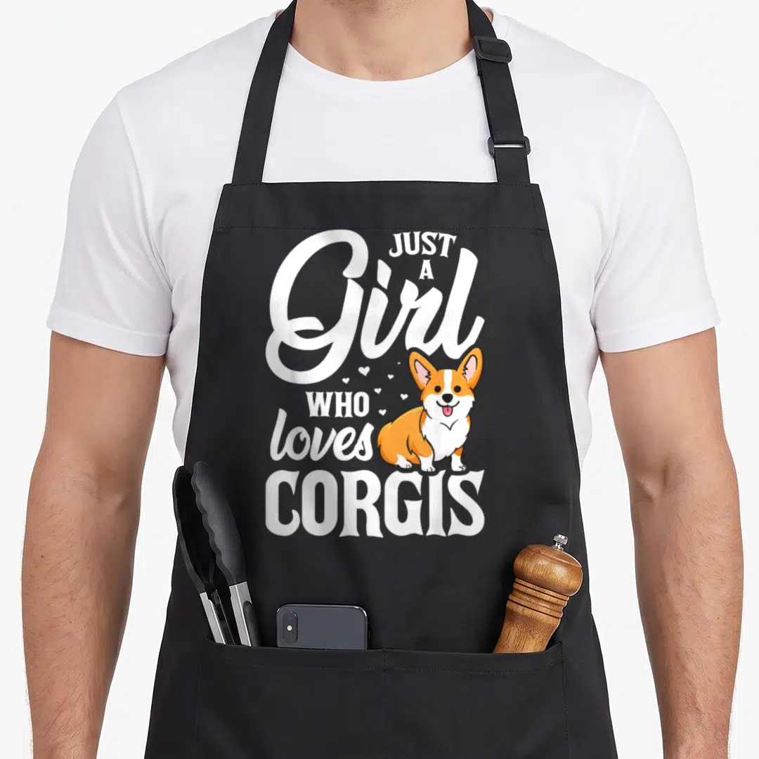 Corgis dog apron - Cartoon corgi with white text wrapping around it and small hearts scattered on grey background — shown on a black cotton canvas apron against a white background