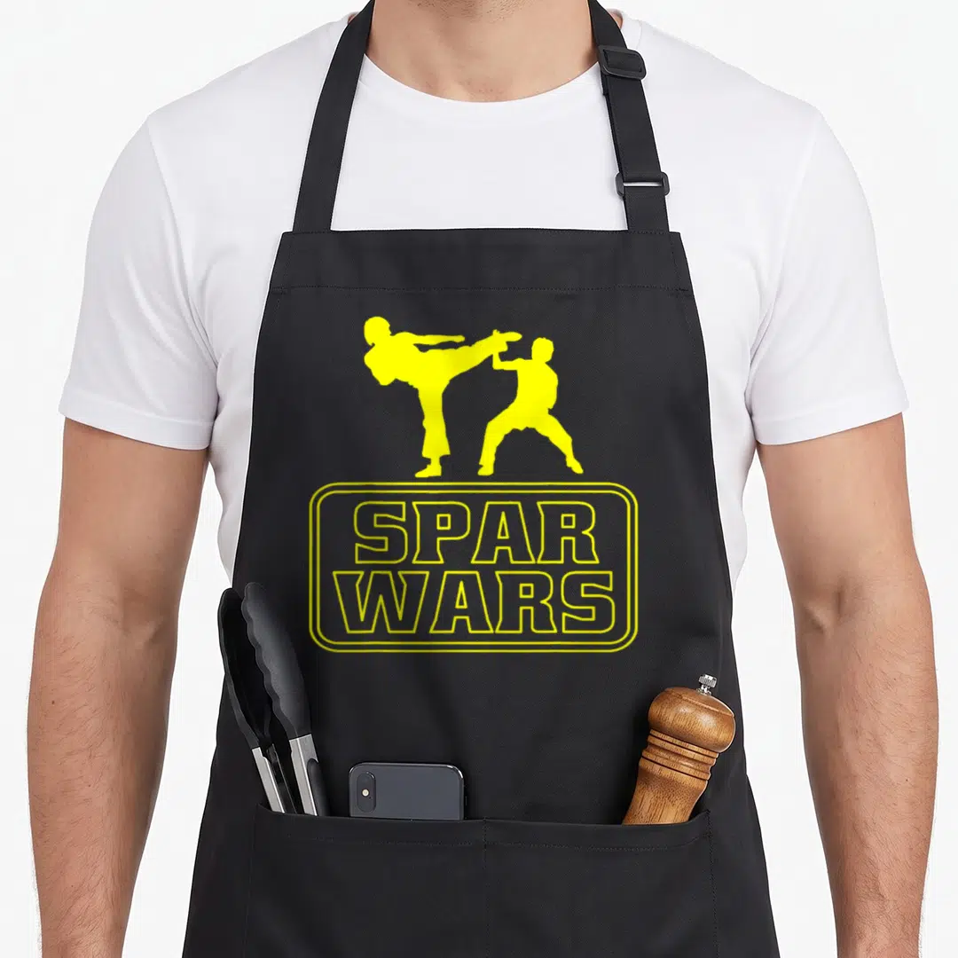 Funny taekwondo martial apron - Two yellow martial artist silhouettes above SPAR WARS text in rounded border — shown on a black cotton canvas apron against a white background