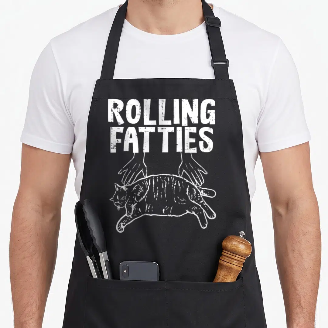 Rolling fat man in apron - White text Rolling Fatties above two hands rolling a cat in line art — shown on a black cotton canvas apron against a white background