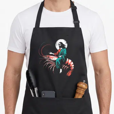 Riding christian apron - Haloed figure wearing sunglasses riding a large red and white shrimp in distressed art style — shown on a black cotton canvas apron against a white background
