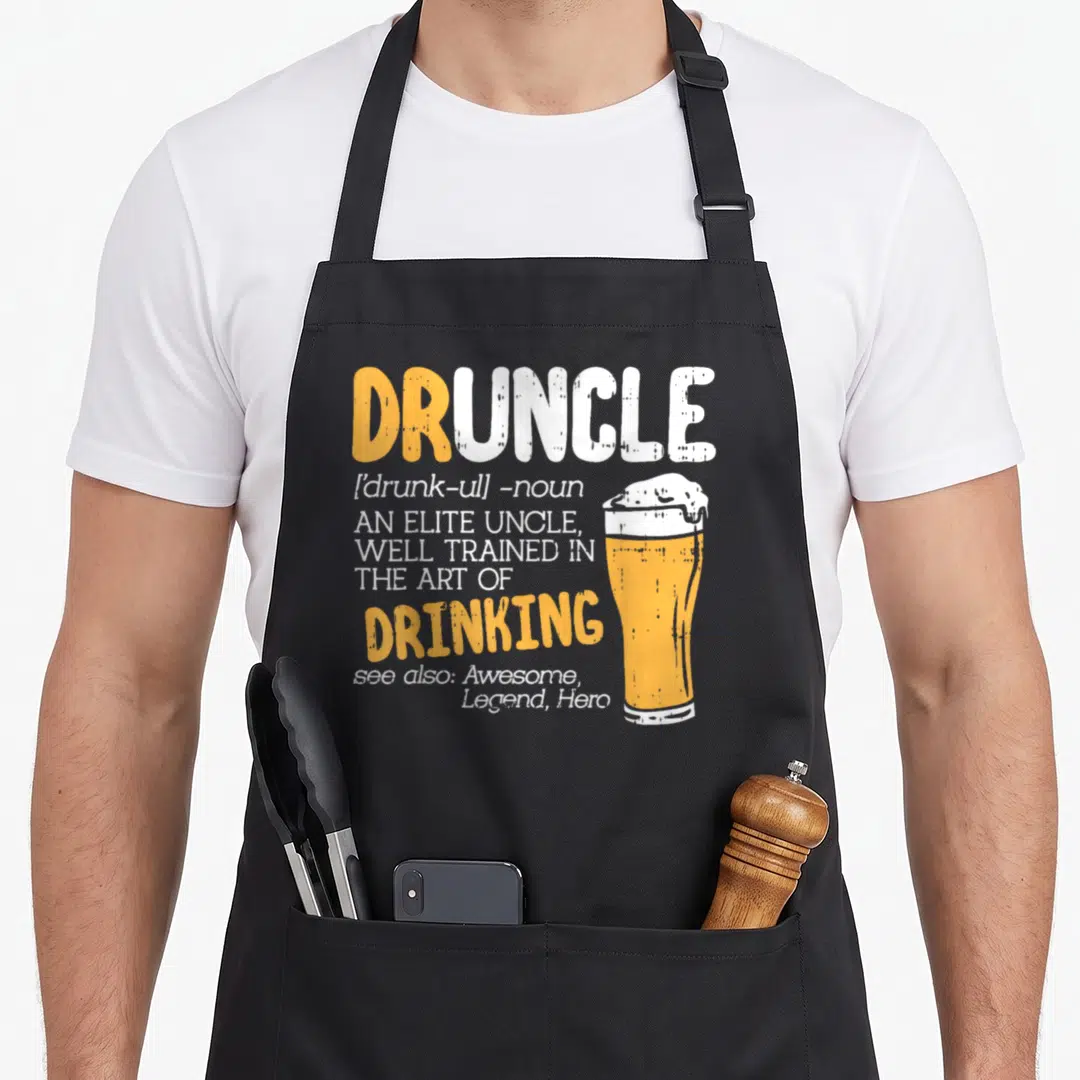 Boredkoalas art husband apron - Orange and white Druncle dictionary text next to a glass of beer with foamy head — shown on a black cotton canvas apron against a white background