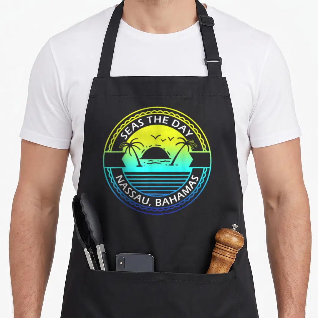 Cute proud bahamian apron - Circular beach emblem with palm trees sun birds and SEAS THE DAY NASSAU BAHAMAS text — shown on a black cotton canvas apron against a white background