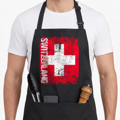 Distressed swiss apron - Red square with white cross and vertical SWITZERLAND text in distressed style — shown on a black cotton canvas apron against a white background