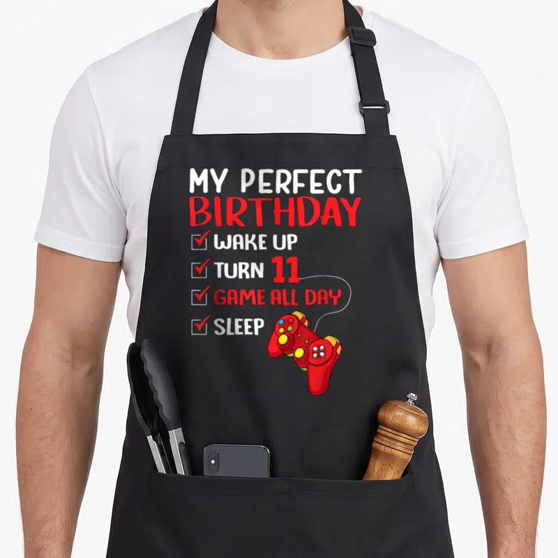 11th gaming aprons - Checklist reading My Perfect Birthday Wake Up Turn 11 Game All Day Sleep with red controller — shown on a black cotton canvas apron against a white background