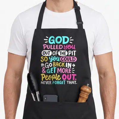 God celebrate apron - Stacked colorful typography reading God Pulled You Out of the Pit So You Could Go Back In Get — shown on a black cotton canvas apron against a white background