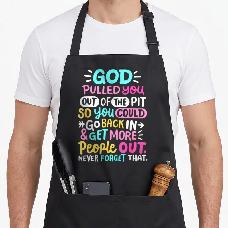 God celebrate apron - Stacked colorful typography reading God Pulled You Out of the Pit So You Could Go Back In Get — shown on a black cotton canvas apron against a white background