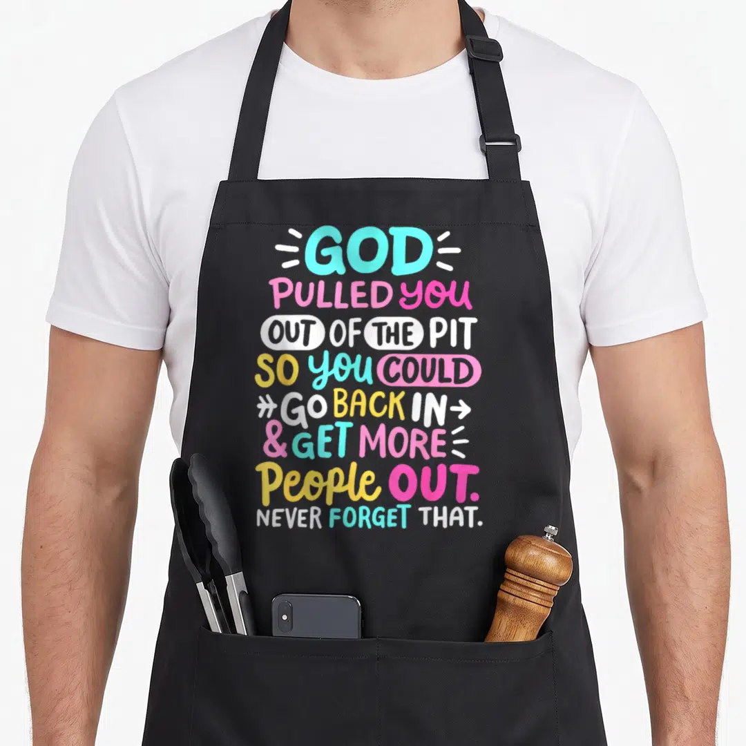 God celebrate apron - Stacked colorful typography reading God Pulled You Out of the Pit So You Could Go Back In Get — shown on a black cotton canvas apron against a white background