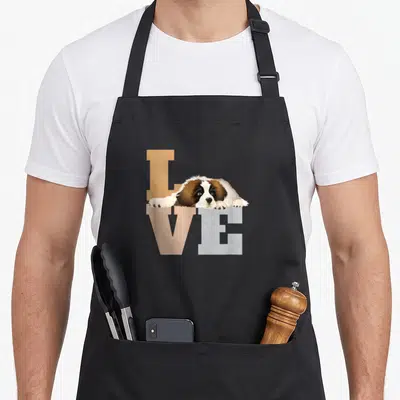 Bernard dog apron - Realistic St Bernard puppy lying across tan and grey LOVE text — shown on a black cotton canvas apron against a white background