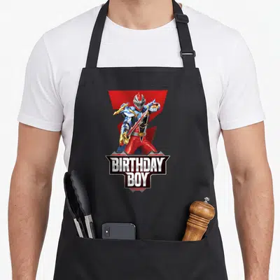Dino birthday apron - Red Power Ranger holding sword with BIRTHDAY BOY text in grey and white banner — shown on a black cotton canvas apron against a white background