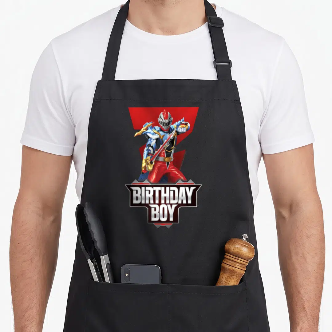 Dino birthday apron - Red Power Ranger holding sword with BIRTHDAY BOY text in grey and white banner — shown on a black cotton canvas apron against a white background