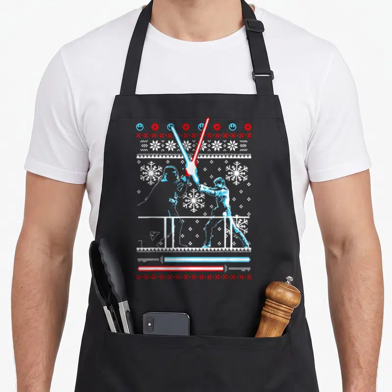 Luke christmas apron - Pixel art two figures dueling with blue and red lightsabers surrounded by white snowflakes — shown on a black cotton canvas apron against a white background