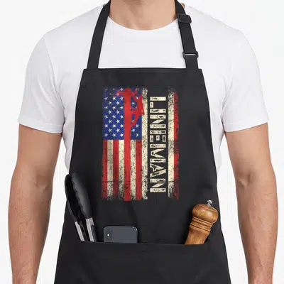 Flag electricians apron - Red lineman silhouette on distressed flag with vertical LINEMAN text — shown on a black cotton canvas apron against a white background