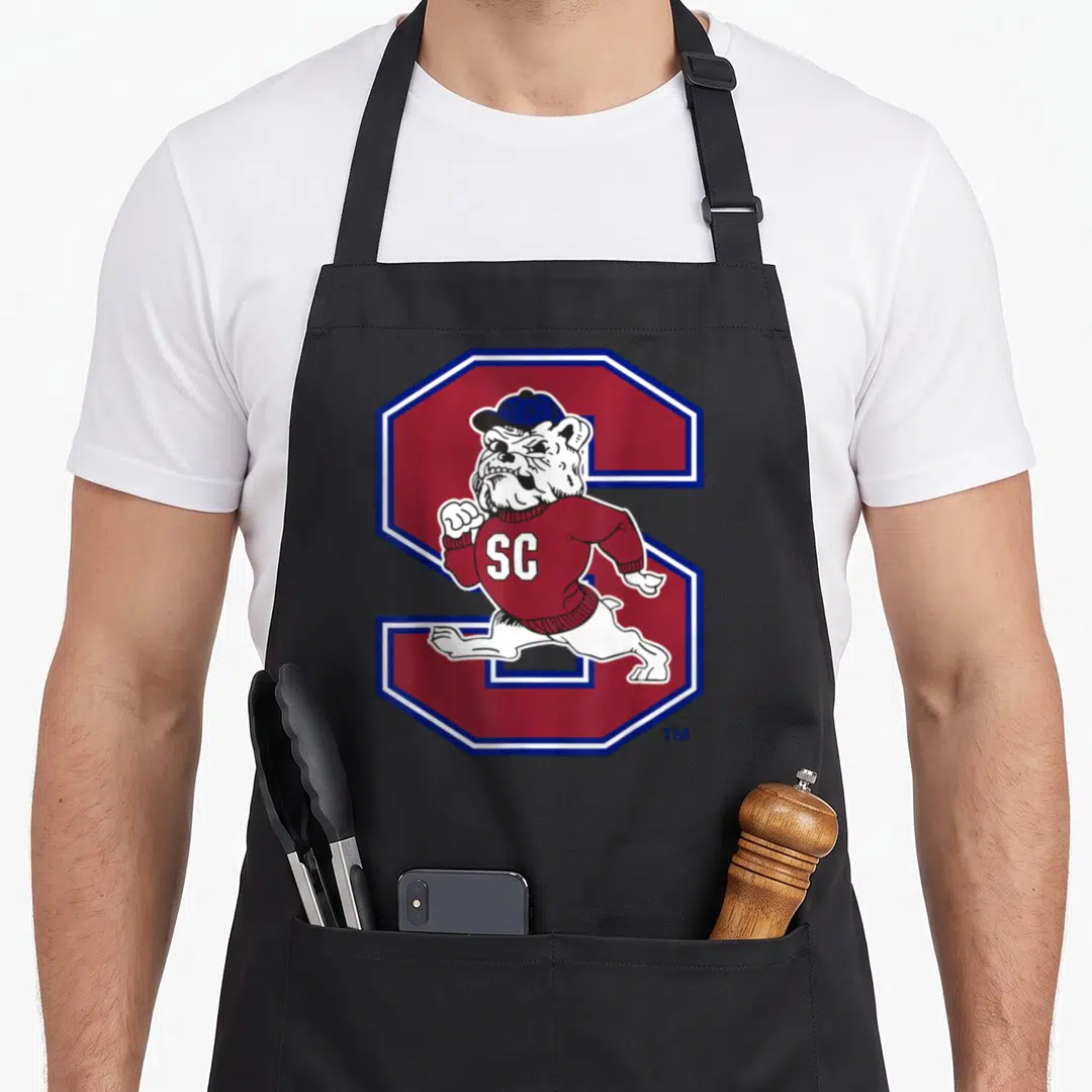 South state university apron - Cartoon bulldog in red sweater running in front of a large red S with blue border — shown on a black cotton canvas apron against a white background