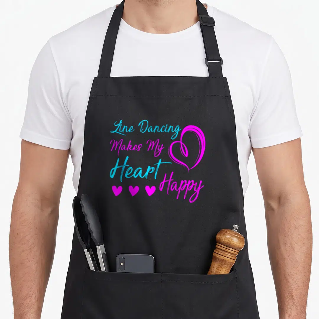 Dancing dance line apron - Stacked blue and magenta text reading Line Dancing Makes My Heart Happy next to a large — shown on a black cotton canvas apron against a white background