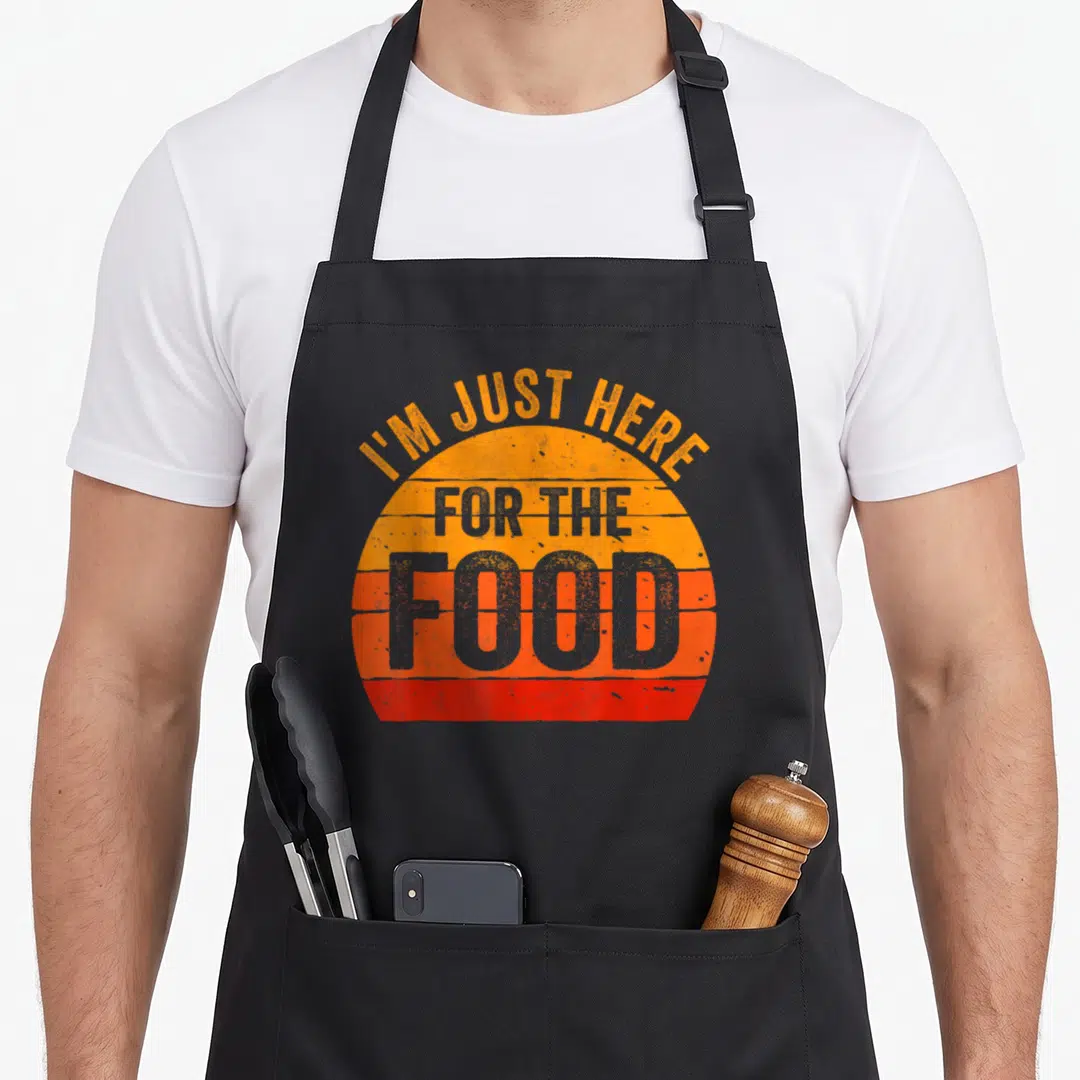 Food thanksgiving day aprons - I'M JUST HERE FOR THE FOOD text over orange red grey striped semi-circle — shown on a black cotton canvas apron against a white background